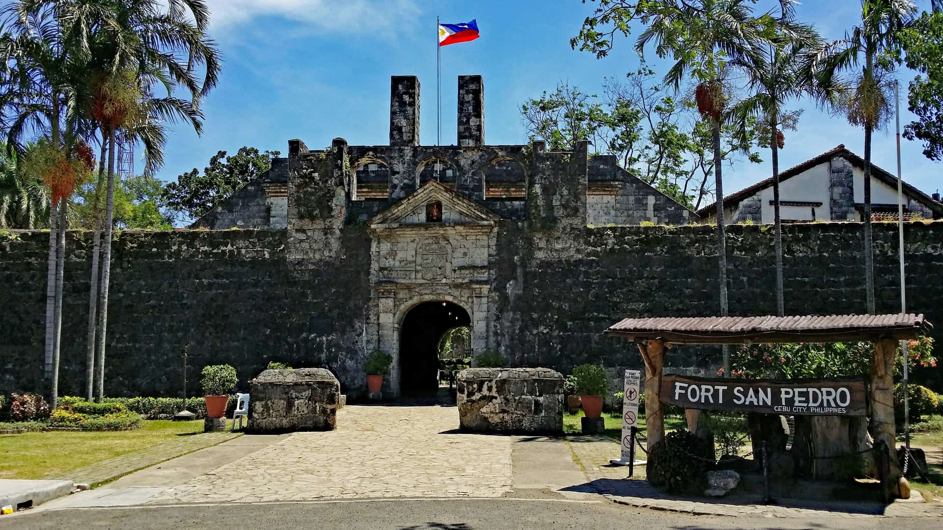 The stone gateway of Fort San Pedro in Cebu City, framed by palm trees under a clear blue sky.